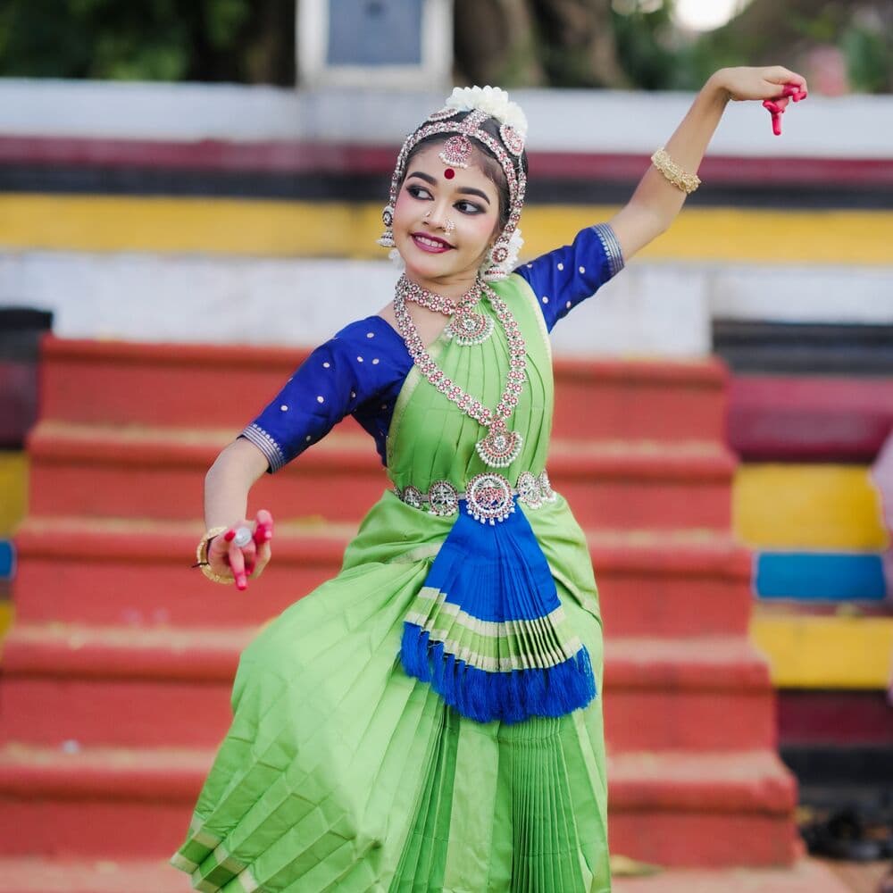 A student dancing outdoors in green and blue costume