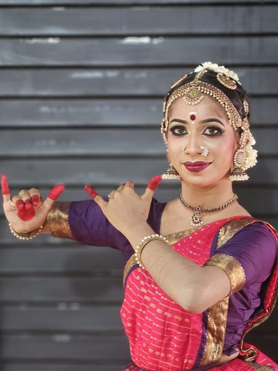 A Bharatanatyam dancer in a pink and purple kasavu costume, hands in a mudra